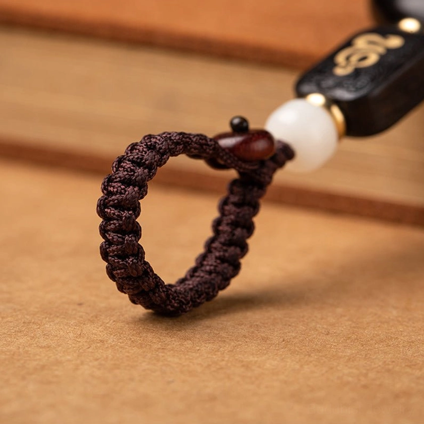 Close-up of braided cord ring and engraved ebony wood plate on Buddhist bodhi lotus keychain showing artisan details
