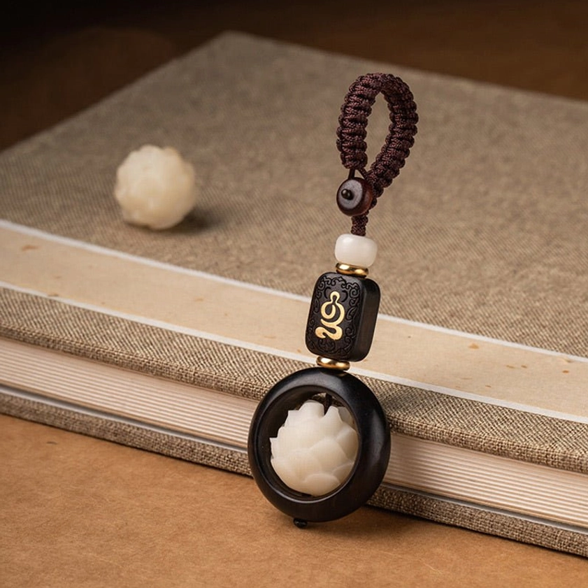 Ebony wood bodhi lotus keychain beside loose bodhi bead on vintage books showing classic Buddhist charm craftsmanship