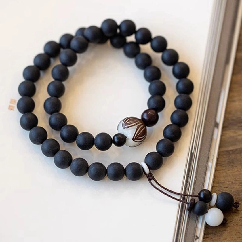 Hand-carved bodhi lotus meditation bracelet on antique book pages showing white inlay detail and tassel charm