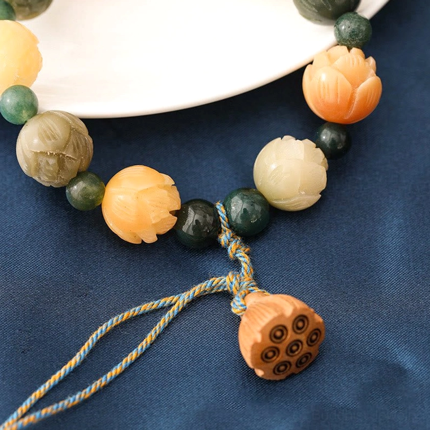 Bodhi seed lotus bracelet side view with braided tassel and large engraved lotus pod pendant on white plate