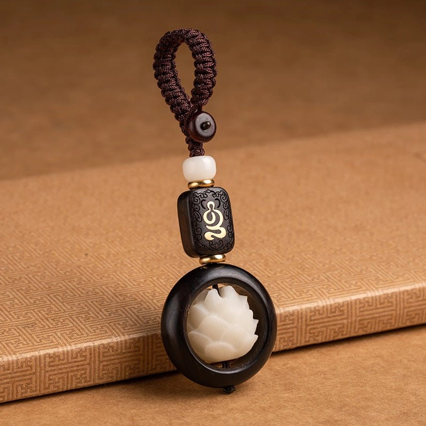 Single handcrafted Buddhist bodhi seed lotus keychain with rotating white lotus pendant and wooden beads on textured wooden table