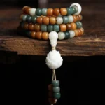 Bodhi lotus mala necklace 108 beads flat lay with carved white lotus pendant on wooden surface
