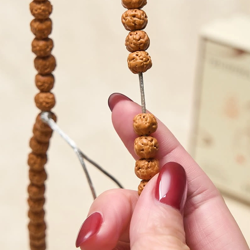 Bodhi seed prayer beads held in fingertips showing two bead sections with silver tassel and red nail polish detail