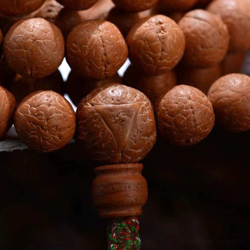 Close-up of Bodhi prayer beads showing seed eye patterns, wooden guru bead, and green woven tassel