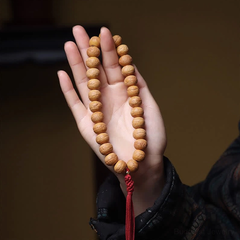 Phoenix Eye Bodhi Buddhist mala beads resting on open palm, displaying natural seed texture and tassel