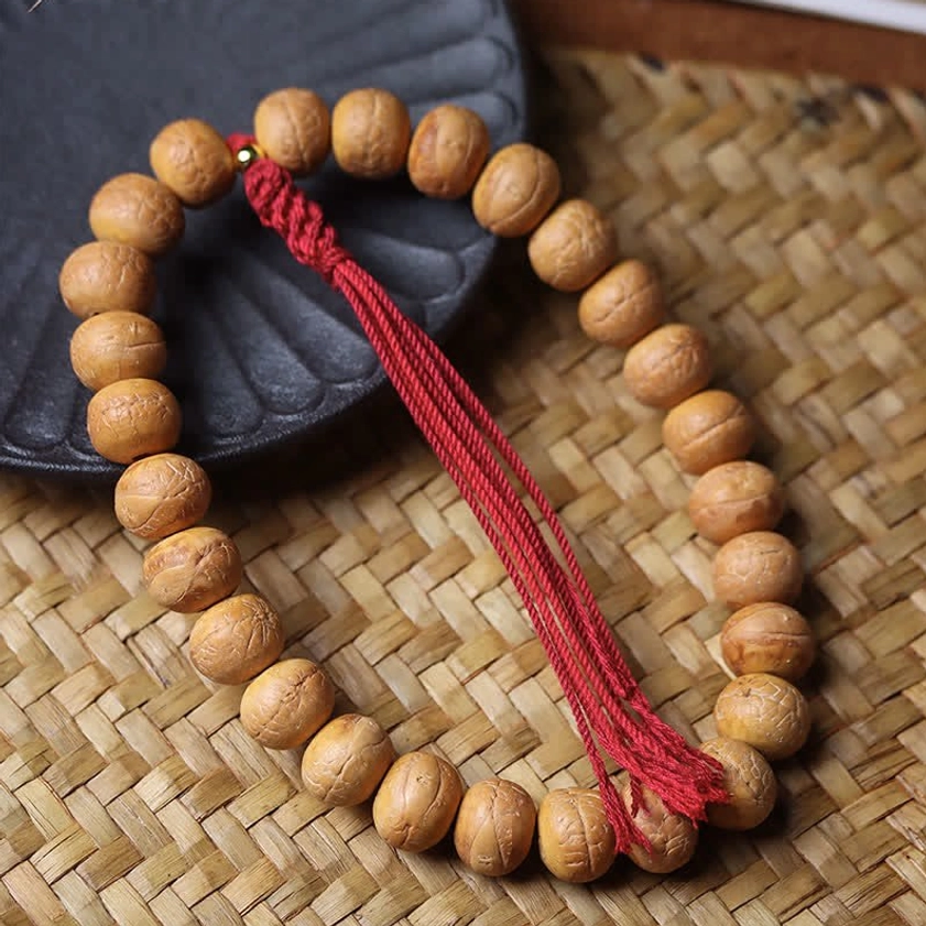 Top-down view of authentic Phoenix Eye Bodhi prayer beads mala with red silk tassel on woven bamboo surface