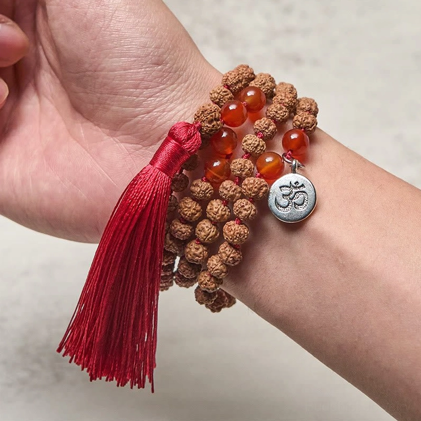 Bodhi seed mala beads worn on wrist close-up showing om charm and red tassel wearable meditation beads