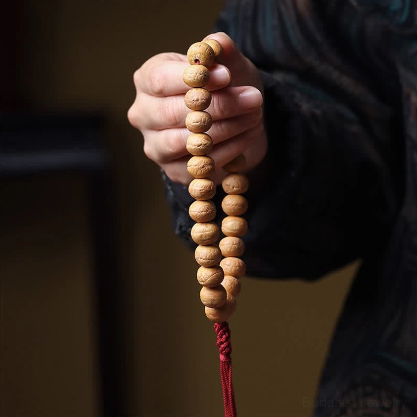 Vertical side view of Phoenix Eye Bodhi mala held in two hands showing bead strand and red tassel