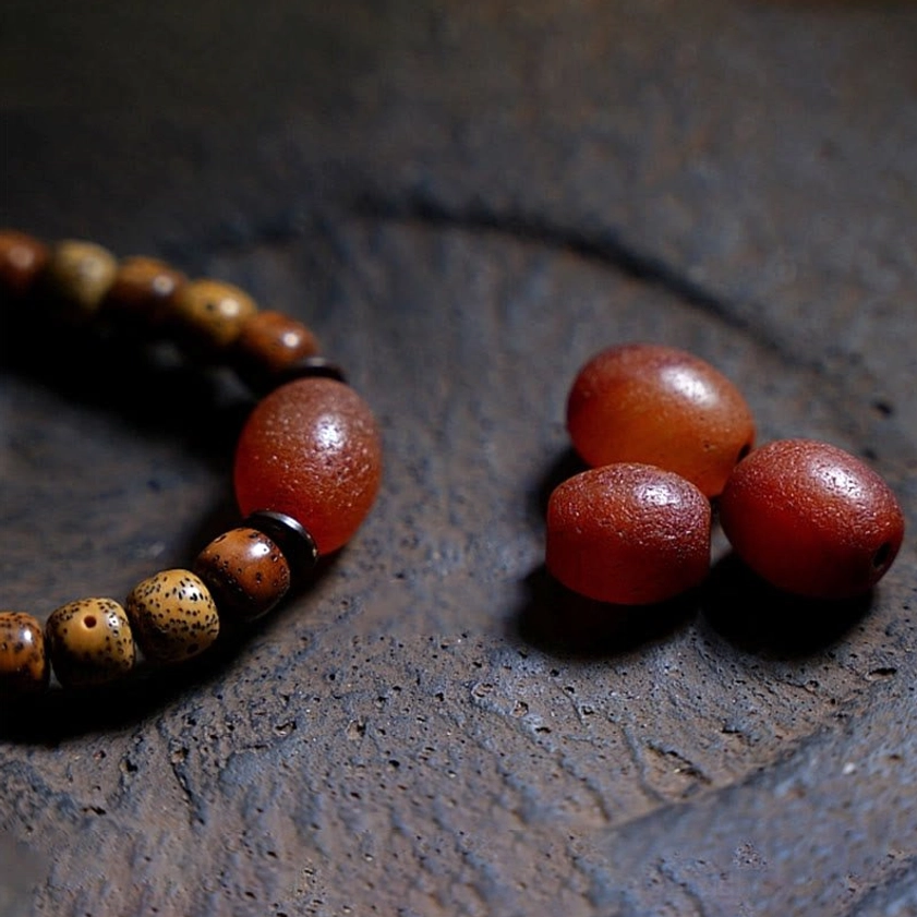 Partial bodhi seed mala bracelet with loose polished red agate round beads on dark stone tabletop