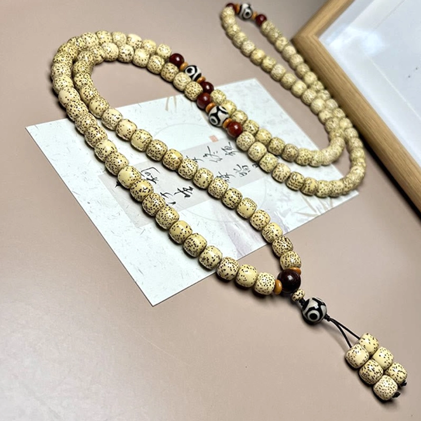 Bodhi seed mala necklace flat lay with draped beads, dark brown sandalwood spacers and protective Dzi bead tassel on desk mat