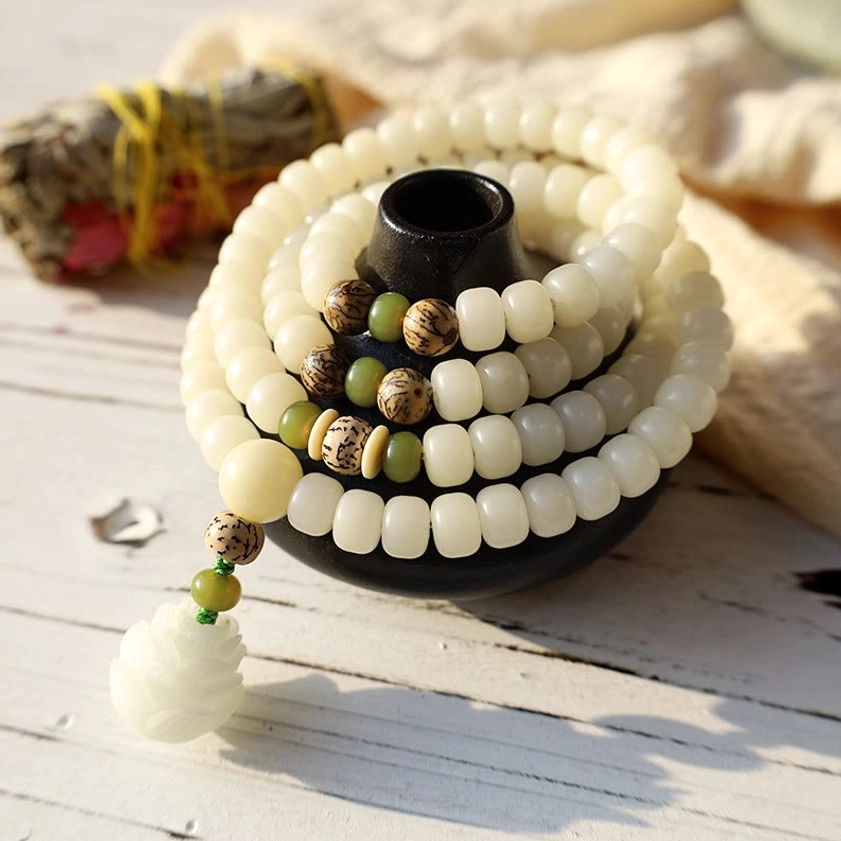 Coiled white bodhi prayer mala in black bowl holder with lotus pendant on wooden table