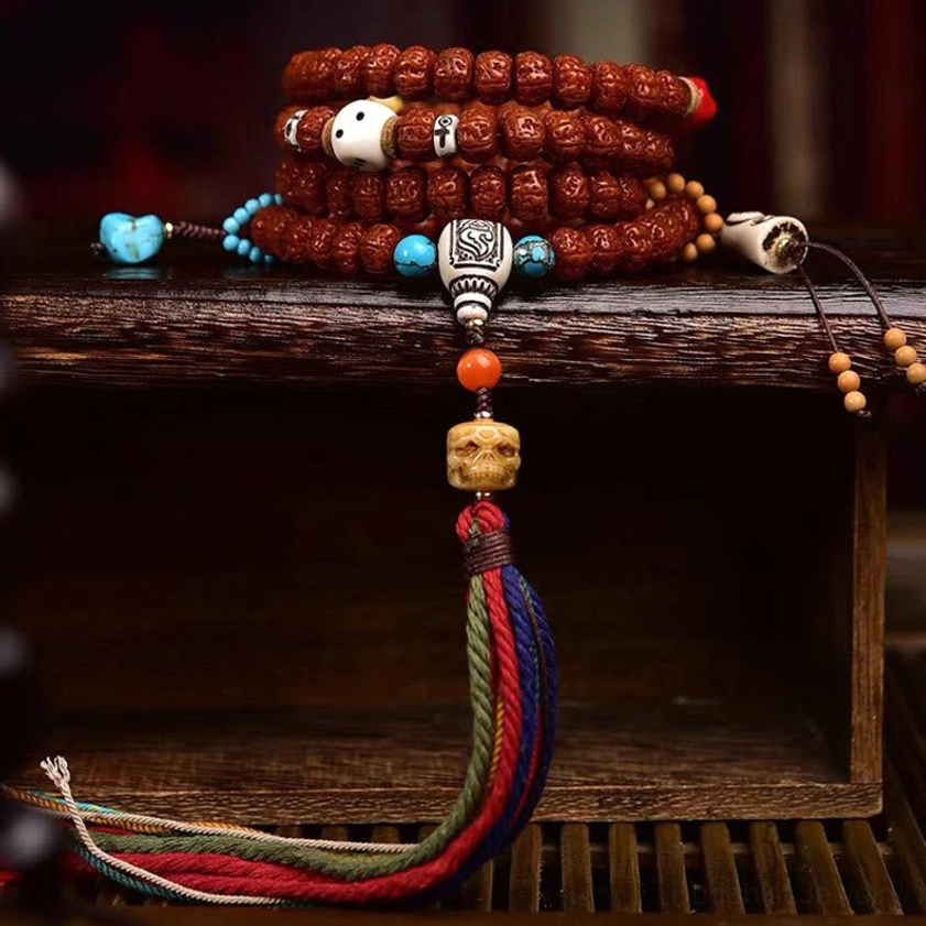 Stacked rudraksha bodhi seed mala bracelets with blue and orange accent beads and long multicolor tassel pendant on wooden display
