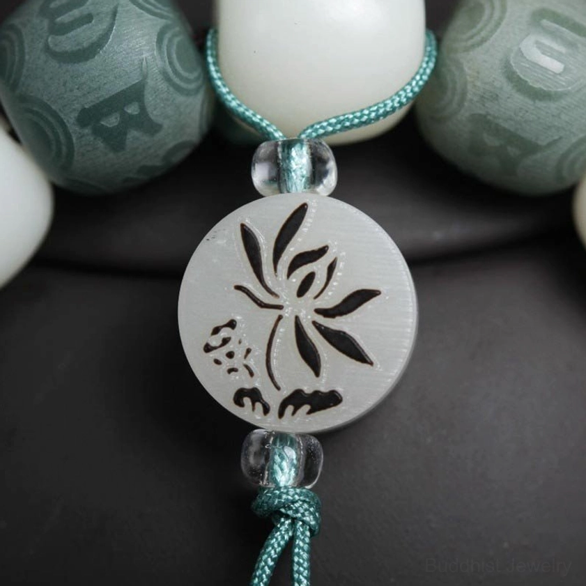 Macro close-up of white bodhi seed bracelet showing carved green mantra beads, lotus pendant detail, and intricate craftsmanship