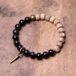 Bodhi seed and black obsidian Buddhist peace bracelet with brass accent on wooden table flat lay