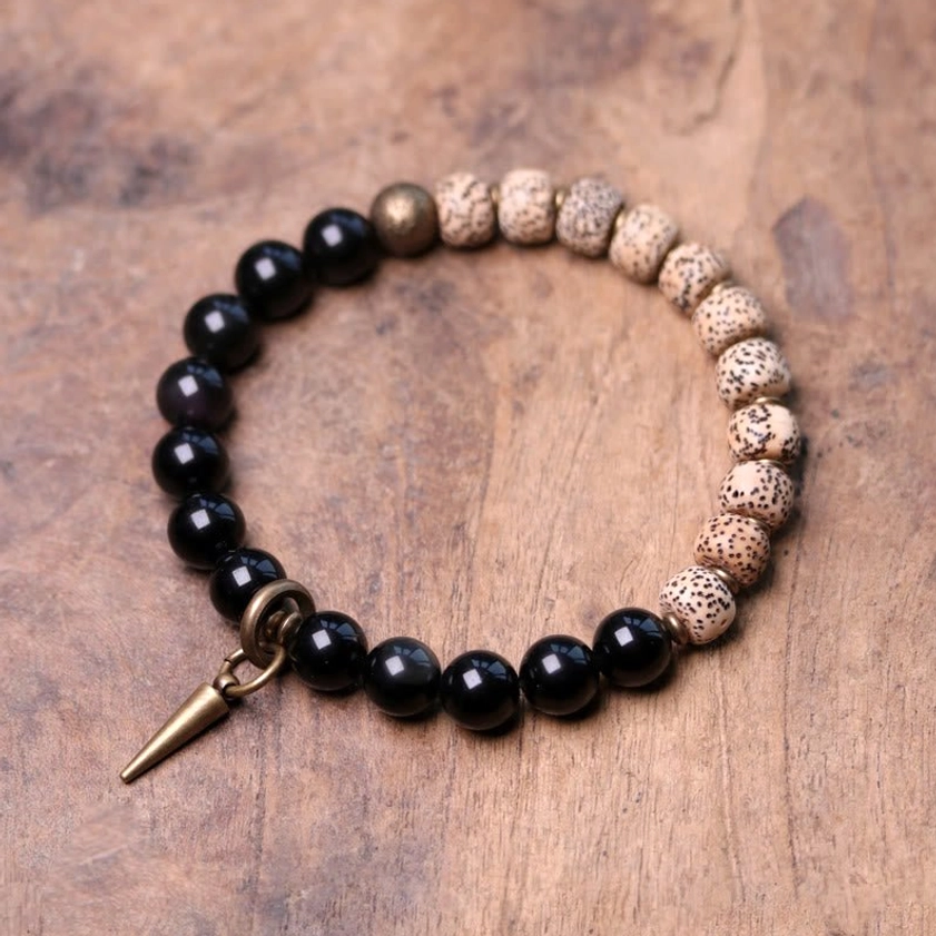 Bodhi seed and black obsidian Buddhist peace bracelet with brass accent on wooden table flat lay