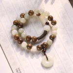 Bodhi seed and green sandalwood double wrap meditation bracelet with white peace buckle charm on Buddhist scripture background, handmade zen jewelry