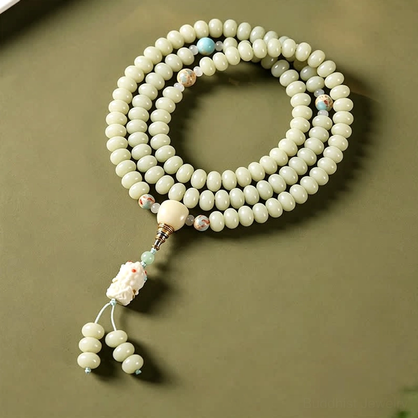 108 prayer mala beads flat lay display with matte white bodhi seeds, guru bead, and Tara pendant on olive green background