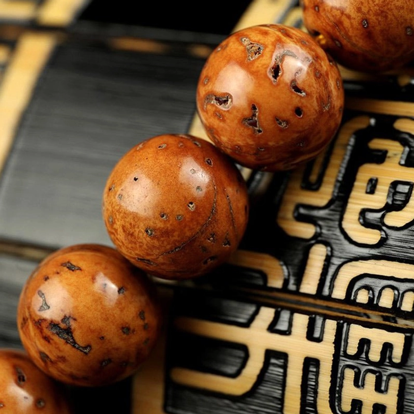 Large bodhi seed beads low-angle close-up macro photography showing tan spotted seeds natural surface pores and authentic texture on Chinese character carved backdrop