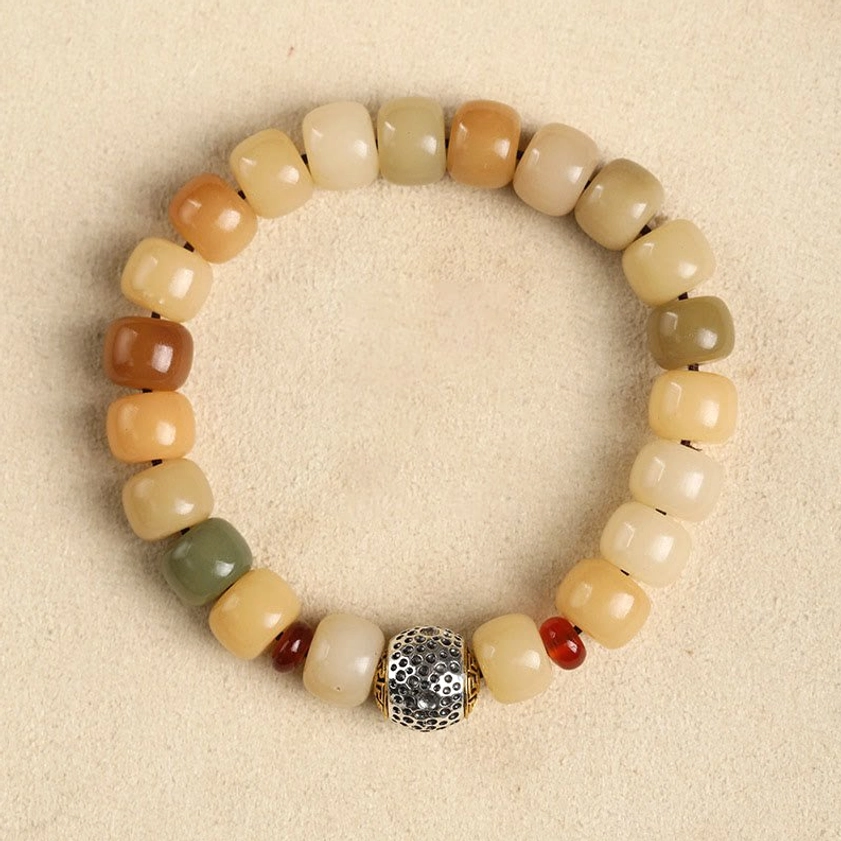 Bodhi seed beaded bracelet overhead flat lay on neutral beige tabletop background with multitone earthy beads, carved silver focal bead with red spacers
