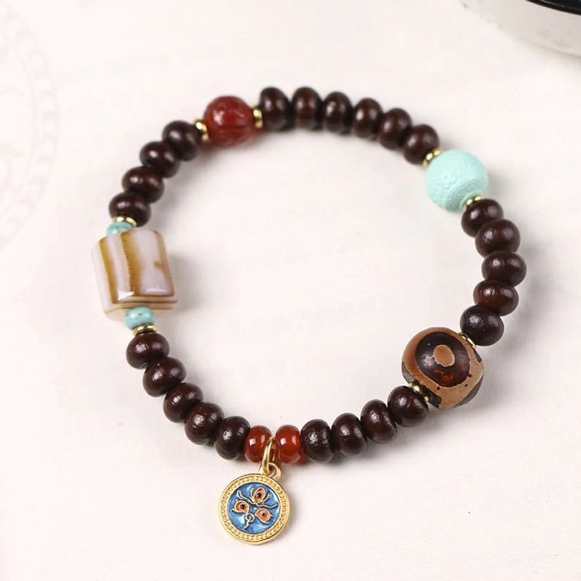 Handmade Buddhist bracelet featuring purple bodhi seeds and striped agate square bead on white background