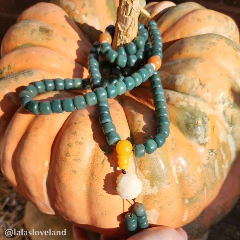 Close-up side view of bodhi seed bracelet showing teal beads, yellow spacer, and white lotus pendant detail