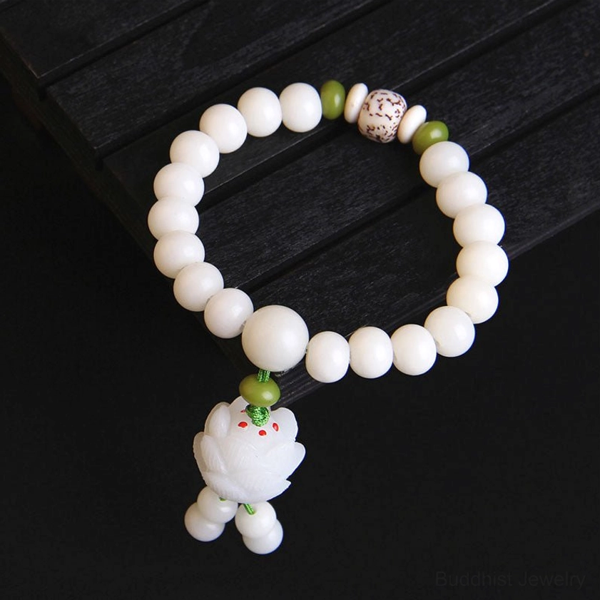 Natural Bodhi seed bracelet for spiritual awakening showing matte white round beads, patterned accent bead, green spacer, and lotus tassel pendant on dark wood surface