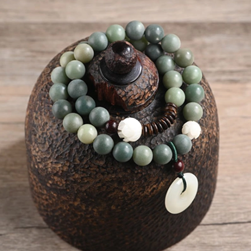 Flat lay display of cyan bodhi seed double wrap bracelet with gradient green beads, white lotus charms, and jade peace buckle on wooden surface