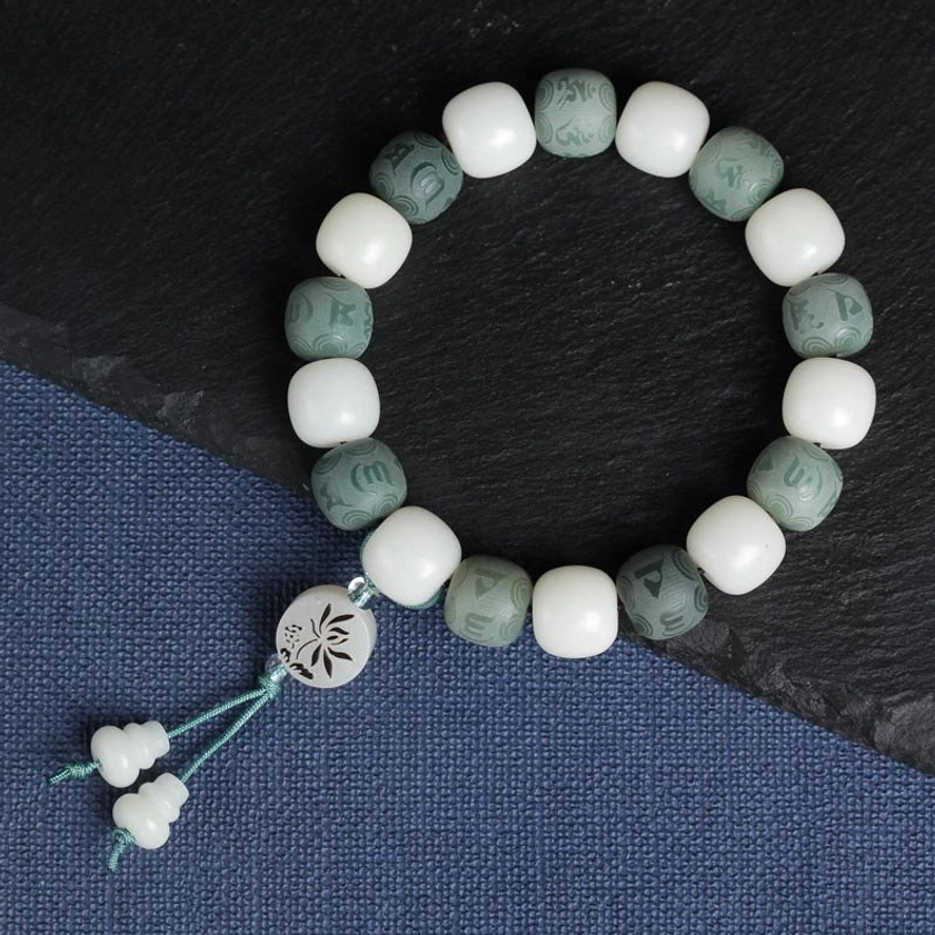 Flat lay photography of white bodhi protection bracelet with lotus pendant charm and double gourd tassel on fabric backdrop