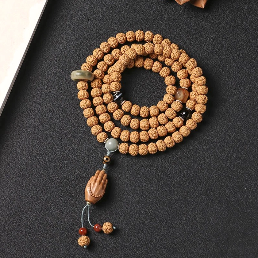 Top-down flat lay view of coiled bodhi seed wealth bracelet with jade accent bead and Buddha hand charm on dark background