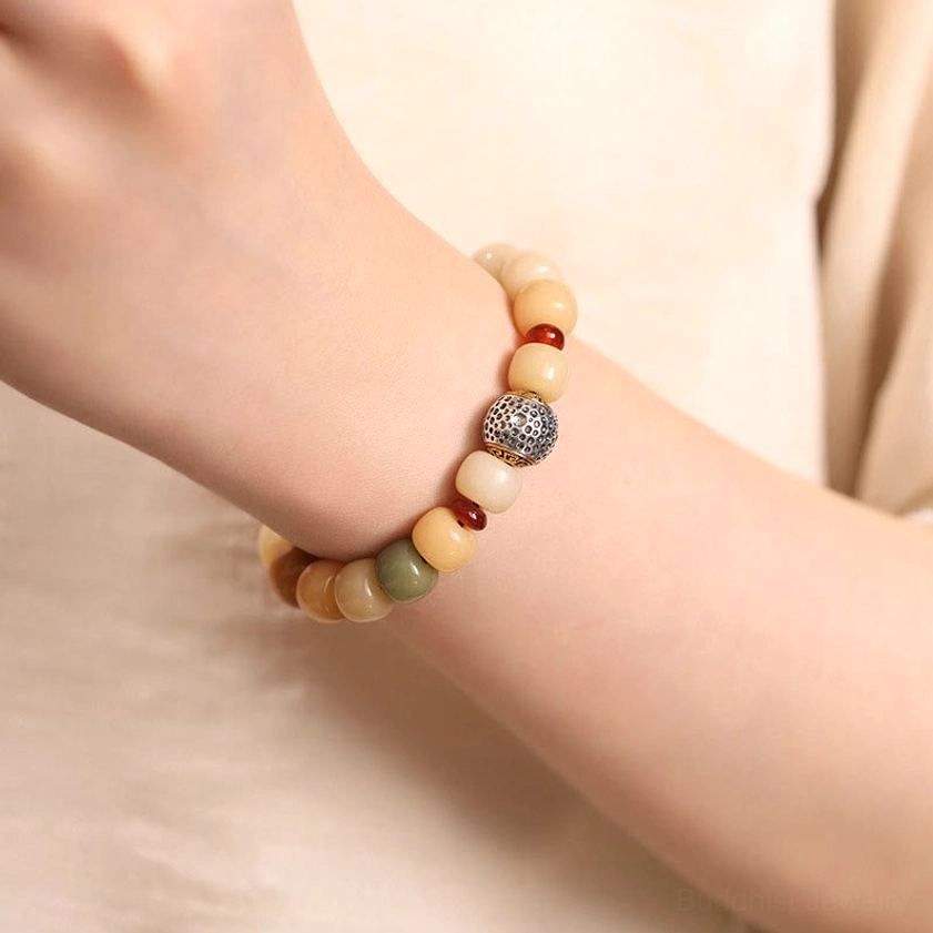 Bodhi seed bracelet worn on hand and wrist close-up view with earthy tone barrel beads and carved silver accent bead against soft fabric backdrop