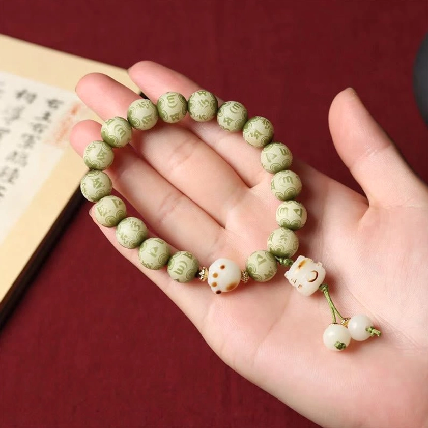 Hand-held display of green Bodhi seed bracelet with cat paw charms resting on palm against red fabric background