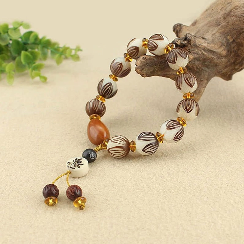 Side oblique shot of bodhi seed meditation bracelet with lotus carved beads and gold-accented tassel charm on driftwood