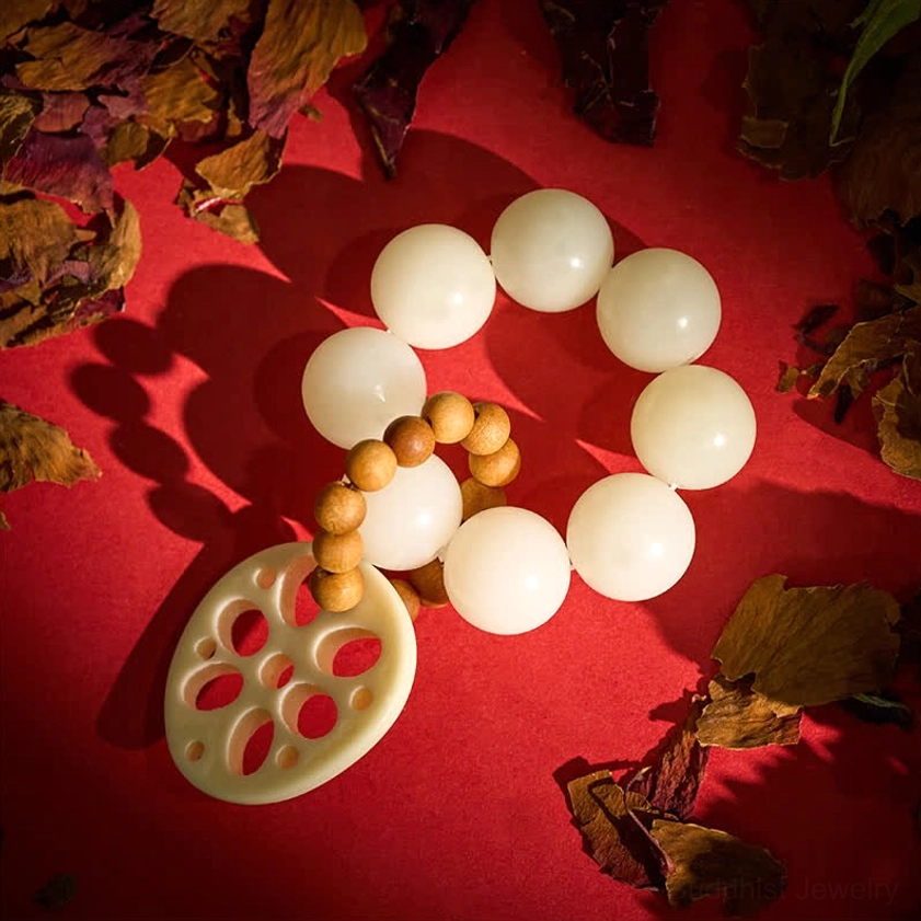 White bodhi seed prayer beads with carved lotus root charm flat lay on red fabric with dried leaves