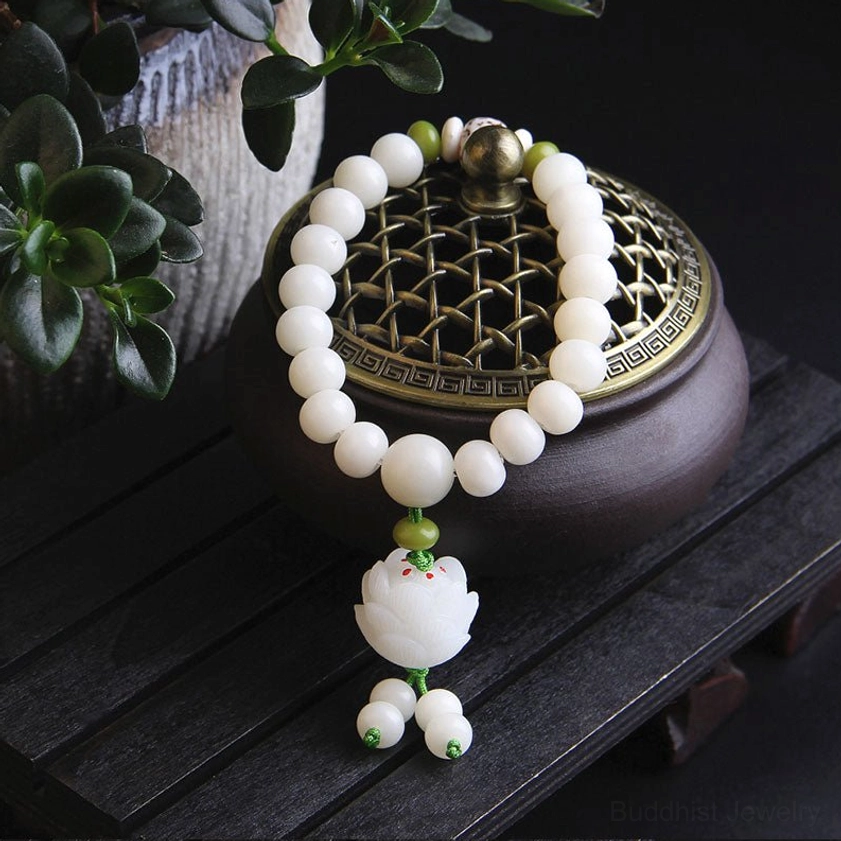Bodhi seed Buddhist bracelet overhead front view with round white beads, green spacer beads, lotus pendant, and incense burner prop on dark wood table