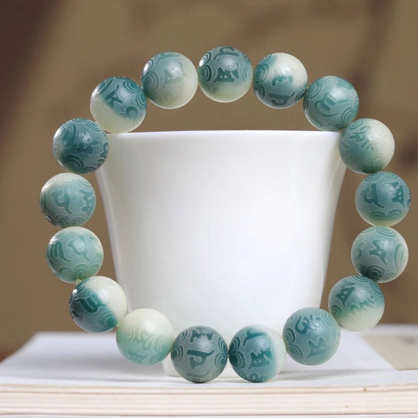 Overhead view of engraved Bodhi seed bracelet with integrated jade spacer ring on ceramic cup