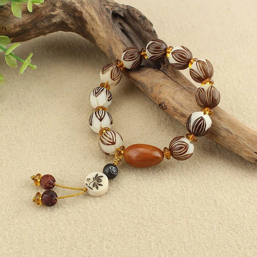Side view of bodhi seed meditation bracelet with lotus carved beads and flower charm tassel on driftwood
