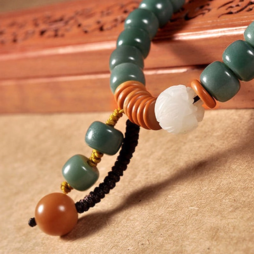 Extreme close-up of bodhi seed beads showing teal color, brown spacers, white lotus charm, and braided tassel