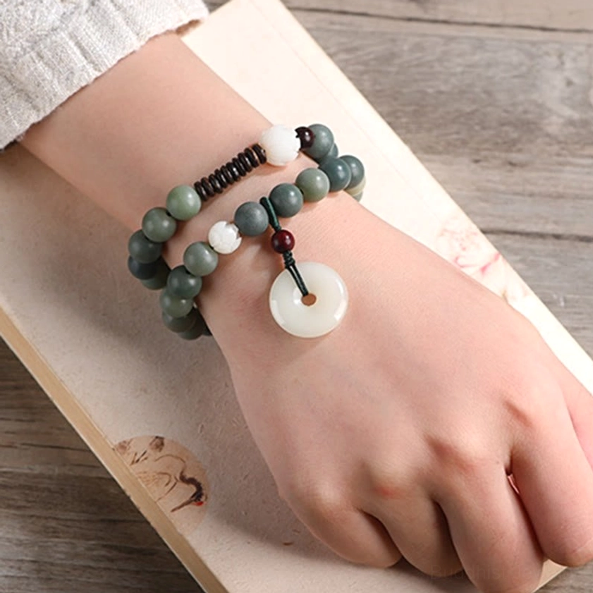 Cyan bodhi seed bracelet on wrist with wooden table and book background, displaying jade peace buckle and double wrap styling