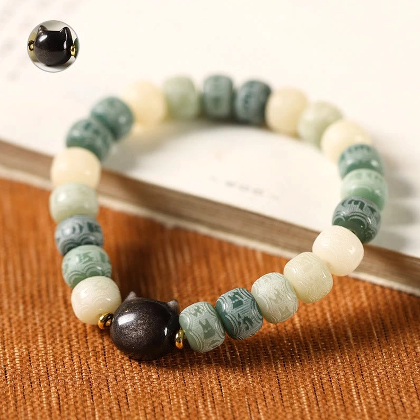 Bodhi seed and obsidian cat bracelet with carved bead details, lifestyle product photography on fabric background
