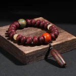 Bodhi seed dzi bead dancing lion bracelet - deep red beads with green patterned dzi stone on dark wooden display