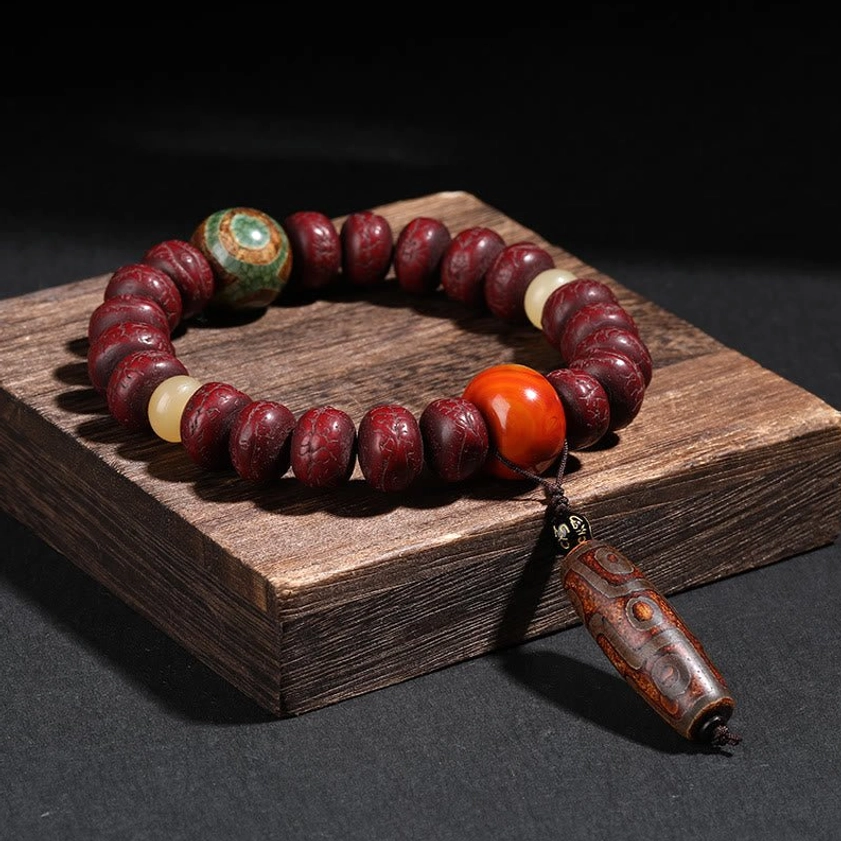 Bodhi seed dzi bead dancing lion bracelet - deep red beads with green patterned dzi stone on dark wooden display