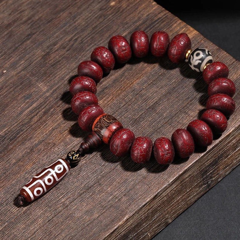 Buddhist bracelet with red bodhi seeds and hand-painted dzi bead pendant on wooden surface