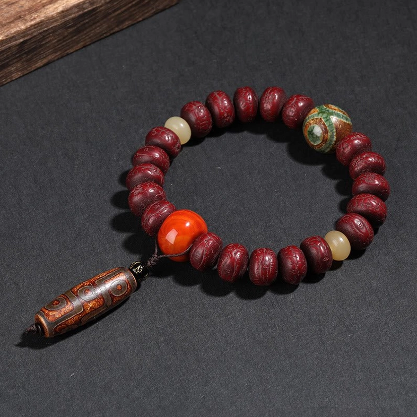 Buddhist meditation mala bracelet flat lay - red bodhi seeds with matching dzi bead pendant on gray background
