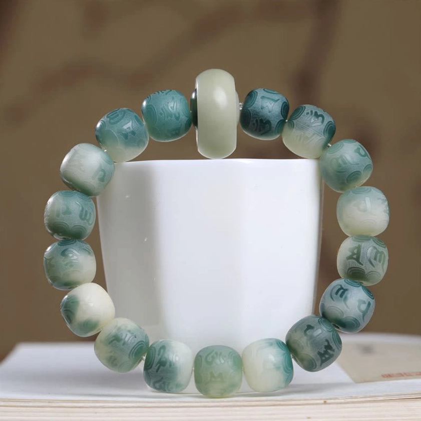 Top-down view of engraved Bodhi seed prayer bracelet with jade spacer ring on white ceramic cup