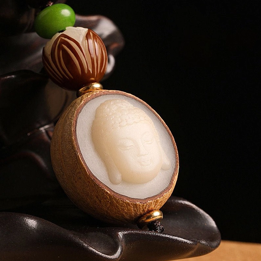 Detailed close-up of carved Buddha face with lotus and green accent beads on wooden background