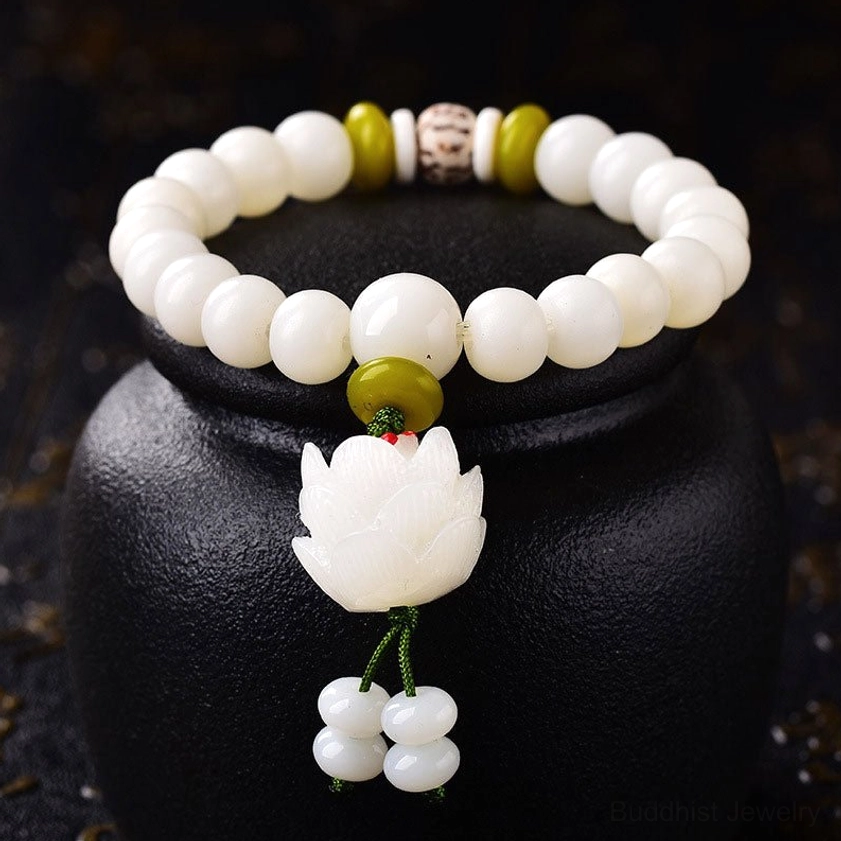 Natural white Bodhi seed bracelet with matte beads, green-yellow spacers, patterned accent bead, and lotus tassel pendant displayed in black ceramic vessel