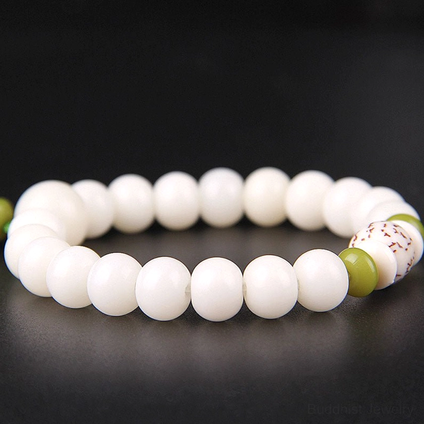 Close-up side view of polished white Bodhi seed bracelet layers showing green and wooden spacers, patterned decorative bead, and lotus charm on dark background