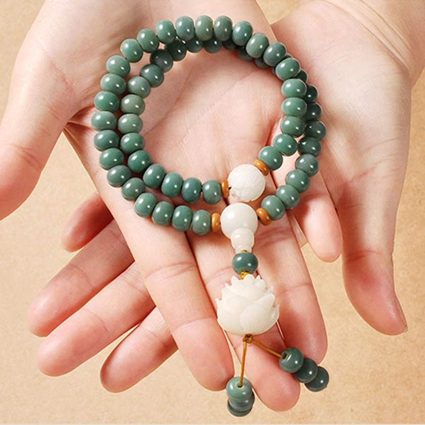 Cyan bodhi seed prayer bracelet held in two hands at eye level, demonstrating double-wrap style with lotus tassel pendant - handmade Buddhist beaded bracelet for enlightenment