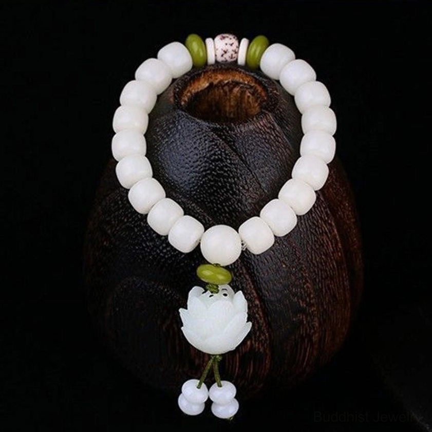 Natural white Bodhi seed Buddhist bracelet three-quarter view on dark wooden craft base, featuring round white beads, green accent beads, and carved lotus tassel pendant