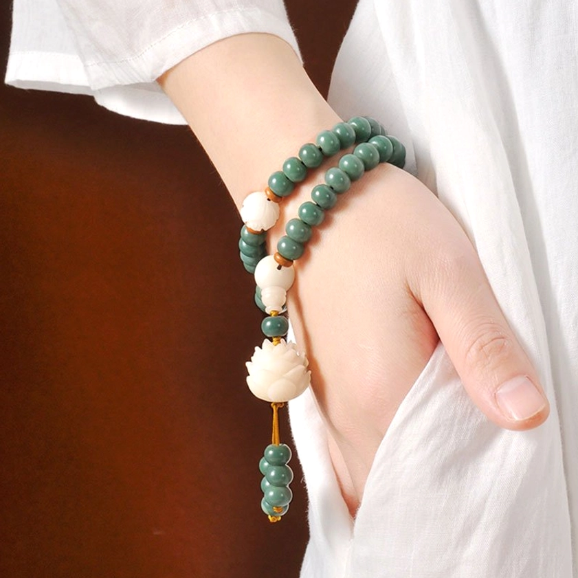 Cyan bodhi seed bracelet worn on wrist in side profile, wrapped double-strand style with hanging lotus charm on brown background - Buddhist spiritual jewelry for daily wear
